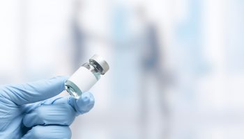 Hand in medical glove holding a vaccine vial